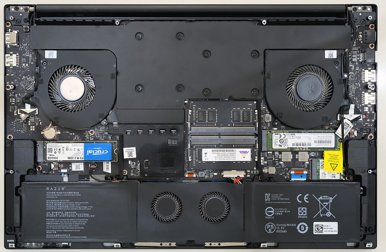 The inside of a laptop with its bottom cover removed: two cooling fans along the top, an M.2 2280 SSD in a slot on the left, two RAM modules in the centre, a second M.2 SSD on the right, and the flat battery pack across the bottom